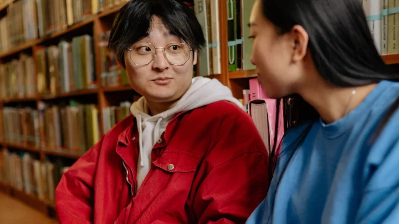 Dua orang membaca di antara rak buku perpustakaan