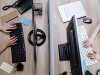 Dua pekerja mengetik di papan ketik komputer pada meja kantor bersekat