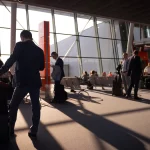 Penumpang dan koper di ruang tunggu keberangkatan bandara yang disinari cahaya pagi