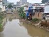 Rumah semipermanen berdiri di tepi Kali Ciliwung yang airnya keruh kecokelatan