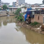 Rumah semipermanen berdiri di tepi Kali Ciliwung yang airnya keruh kecokelatan