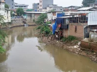 Rumah semipermanen berdiri di tepi Kali Ciliwung yang airnya keruh kecokelatan