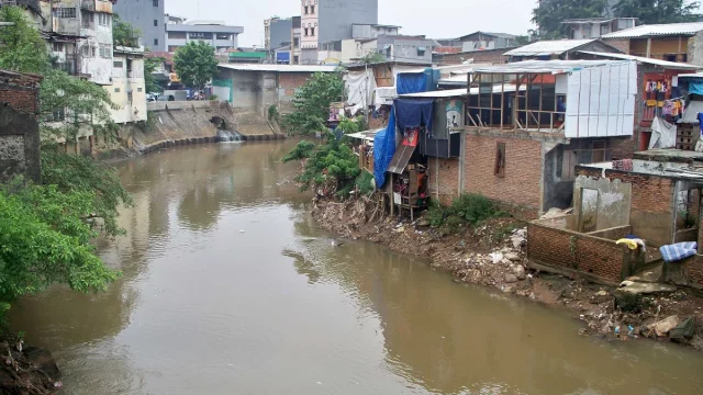 Rumah semipermanen berdiri di tepi Kali Ciliwung yang airnya keruh kecokelatan