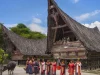Rumah Bolon beratap menjulang dengan rombongan berbusana adat di halamannya