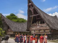 Rumah Bolon beratap menjulang dengan rombongan berbusana adat di halamannya