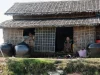 Rumah bambu beratap rumbia dengan tempayan air di tepi sungai, Pyapon, Delta Ayeyarwady, Myanmar