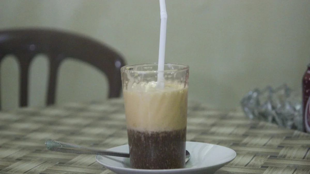 Segelas teh talua bersedotan di atas lepek di meja sebuah warung