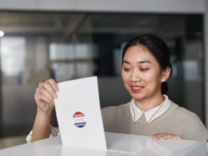 Ilustrasi seorang perempuan memegang surat suara di ruang pemungutan suara.