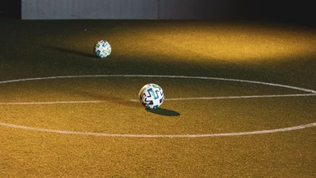 Bola futsal tergeletak di lapangan dalam ruangan bercahaya temaram