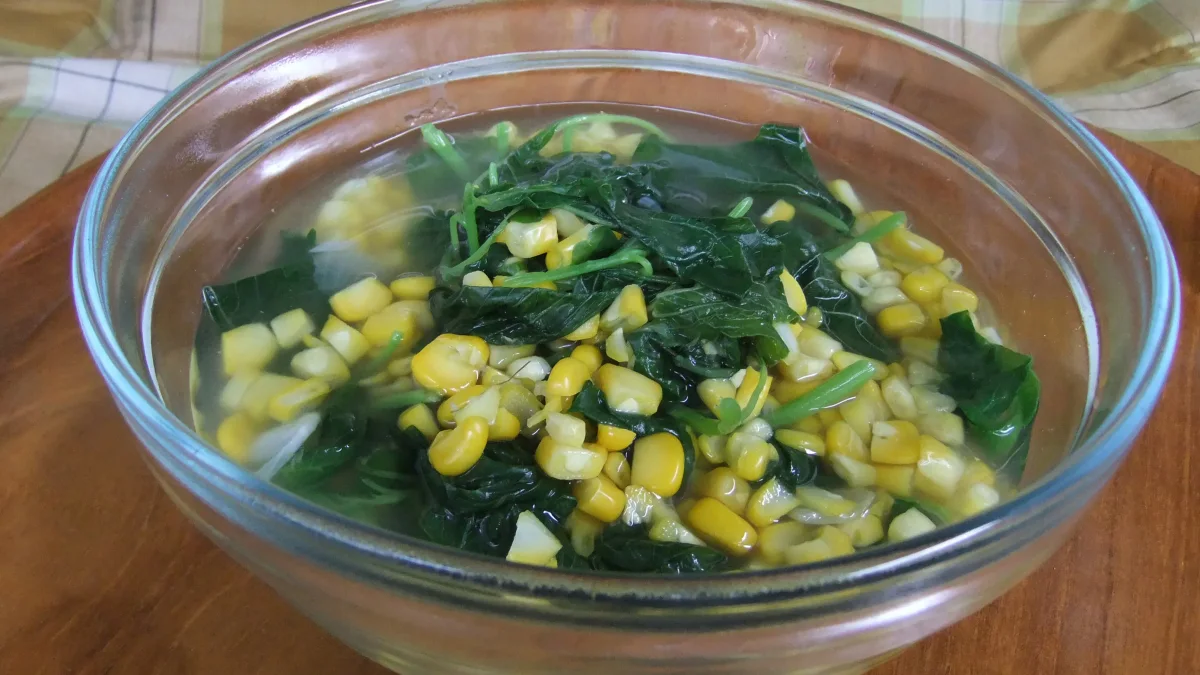 Semangkuk sayur bening bayam dan jagung manis dalam mangkuk kaca di atas meja kayu