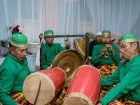 Ilustrasi kelompok pemusik tradisi berbusana hijau memainkan gendang dalam sebuah pertunjukan.