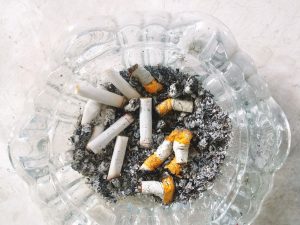 Ilustrasi asbak kaca penuh puntung rokok dan abu.
