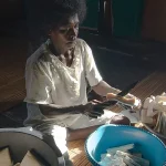 Seorang perempuan memotong sagu kering menjadi balok di samping baskom biru