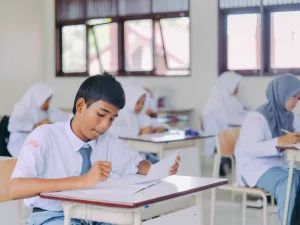 Siswa SMA Indonesia berseragam putih abu-abu menulis dan membaca di meja ruang kelas
