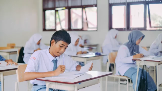 Siswa SMA Indonesia berseragam putih abu-abu menulis dan membaca di meja ruang kelas