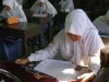 Siswi SMA berseragam putih mengerjakan lembar ujian di ruang kelas.