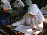 Siswi SMA berseragam putih mengerjakan lembar ujian di ruang kelas.