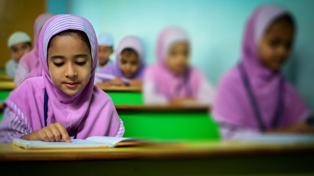 Ilustrasi sejumlah murid perempuan berjilbab menekuni buku di ruang kelas.