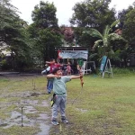 Seorang anak menarik busur panah di lapangan berumput