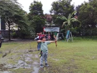 Seorang anak menarik busur panah di lapangan berumput