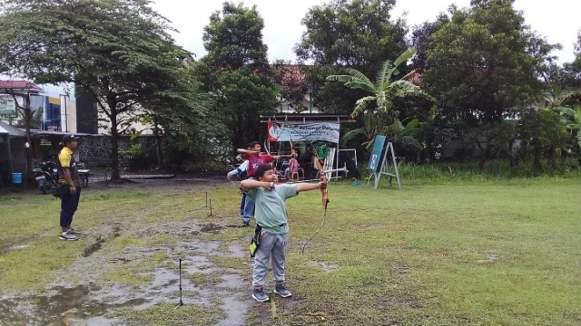 Seorang anak menarik busur panah di lapangan berumput