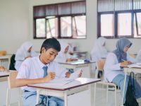 Ilustrasi murid-murid duduk di bangku kelas mengerjakan tugas tulis.