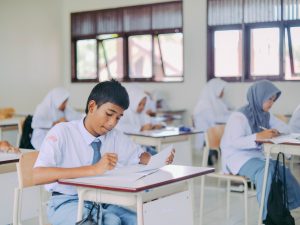 Ilustrasi murid-murid duduk di bangku kelas mengerjakan tugas tulis.