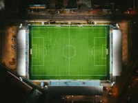 Stadion sepak bola benderang dengan pemain di lapangan dilihat dari udara pada malam hari