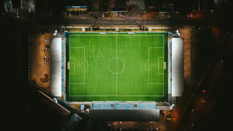 Stadion sepak bola benderang dengan pemain di lapangan dilihat dari udara pada malam hari