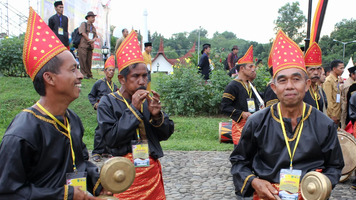Pemain talempong pacik berpakaian adat Minangkabau memainkan gong kecil dan seruling bambu