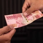Ilustrasi dua tangan bertukar selembar uang Rp100.000
