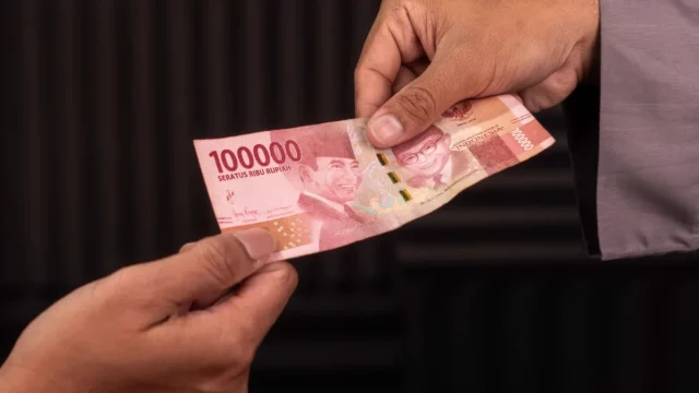 Ilustrasi dua tangan bertukar selembar uang Rp100.000
