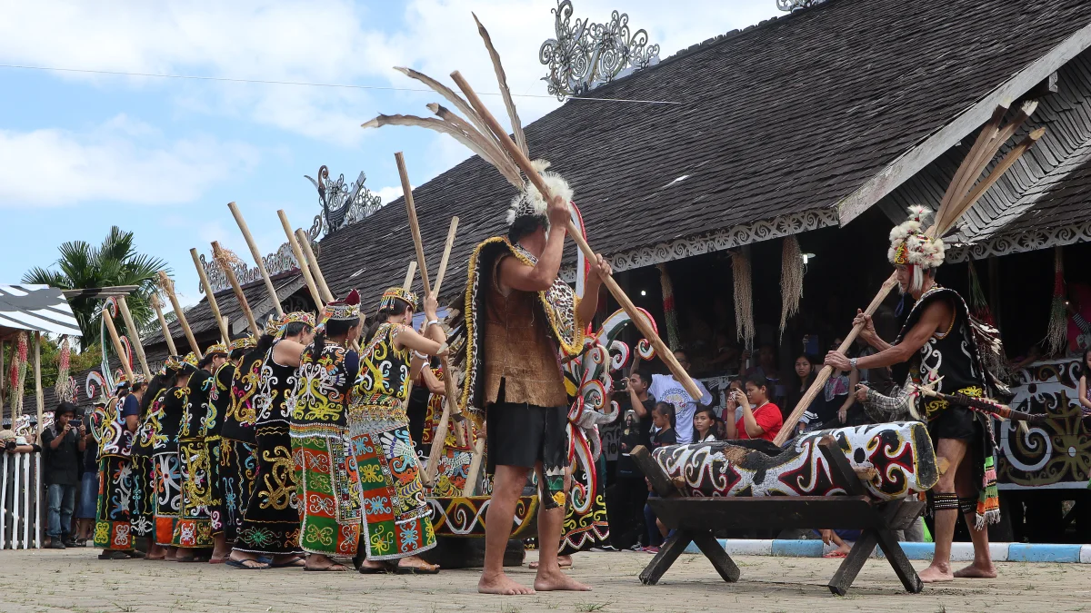 Penari Dayak Kenyah mengangkat tongkat kayu di depan lesung berukir pada Tari Tani