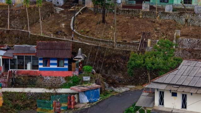 Ilustrasi jalan kampung dengan rumah-rumah warga di kiri dan kanan.