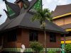 Ilustrasi rumah gadang beratap gonjong berdiri di antara pepohonan.