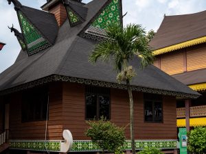 Ilustrasi rumah gadang beratap gonjong berdiri di antara pepohonan.