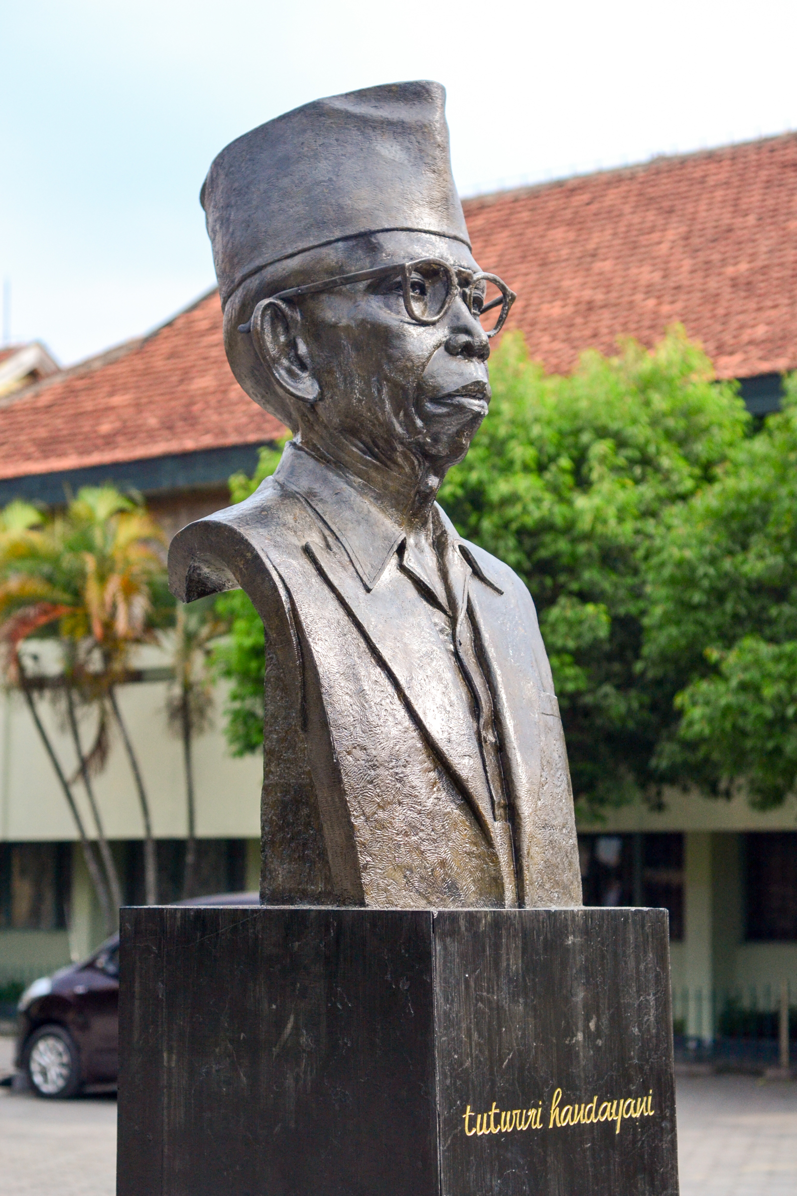 Tembang Wasita Rini dan Kemerdekaan Perempuan 2 Patung dada Ki Hadjar Dewantara bertopi dan berkacamata berdiri di atas tugu batu di halaman berpepohonan.