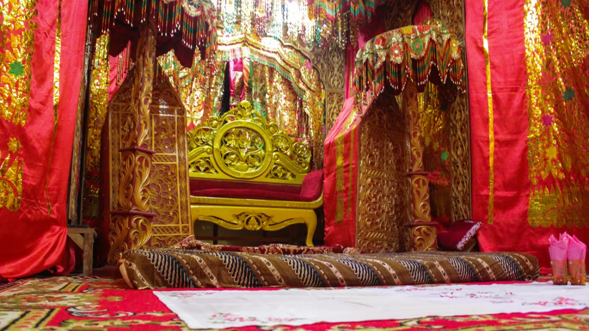 Pelaminan pengantin berhias kain merah dan emas dengan ukiran kayu di belakang kursi