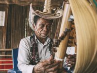 Seorang lelaki berpakaian adat Rote memetik sasando, alat musik dawai berwadah daun lontar.