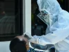 Petugas kesehatan berpakaian APD mengambil sampel swab hidung warga melalui jendela rumah