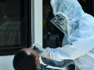 Petugas kesehatan berpakaian APD mengambil sampel swab hidung warga melalui jendela rumah