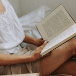 Ilustrasi seorang perempuan membaca buku sambil berbaring santai.