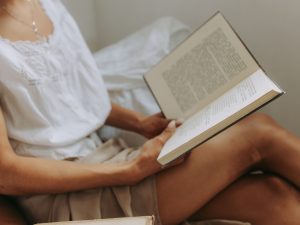 Ilustrasi seorang perempuan membaca buku sambil berbaring santai.