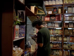 Seorang pria menelusuri rak buku di toko buku kecil berlampu temaram, Yogyakarta