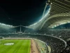 Tribun stadion dipenuhi penonton di bawah lampu terang pada malam hari