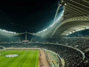 Tribun stadion dipenuhi penonton di bawah lampu terang pada malam hari