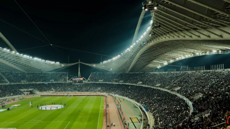 Tribun stadion dipenuhi penonton di bawah lampu terang pada malam hari