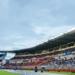 Tribune stadion penuh penonton di bawah lampu sorot