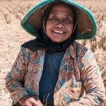 Ilustrasi seorang petani perempuan duduk di petak sawah seusai panen
