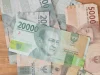 Ilustrasi lembaran rupiah pecahan 20.000 dan 5.000 di atas meja kayu